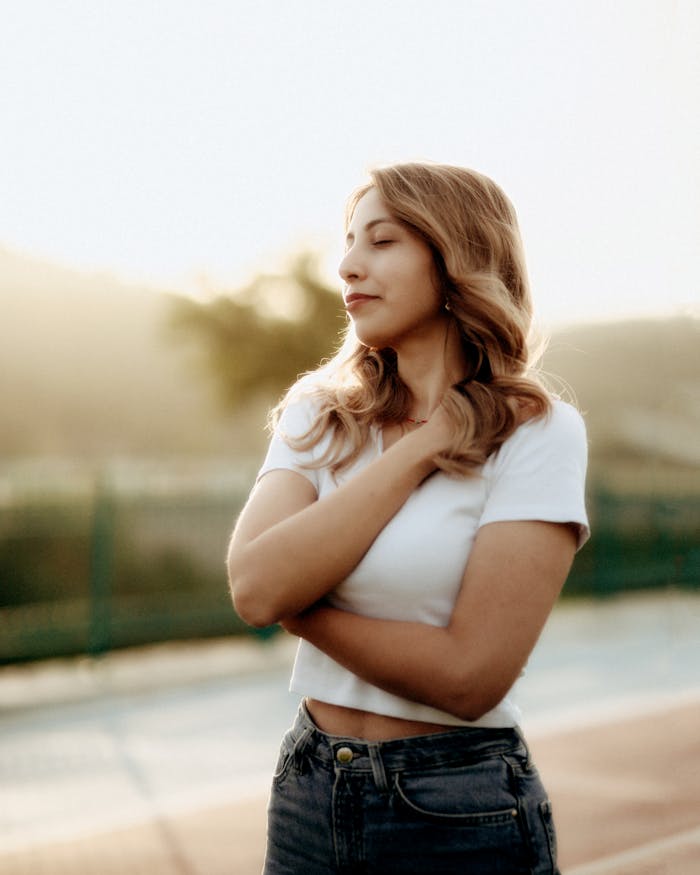 Young woman embracing serenity outdoors during sunset with a soft glow.